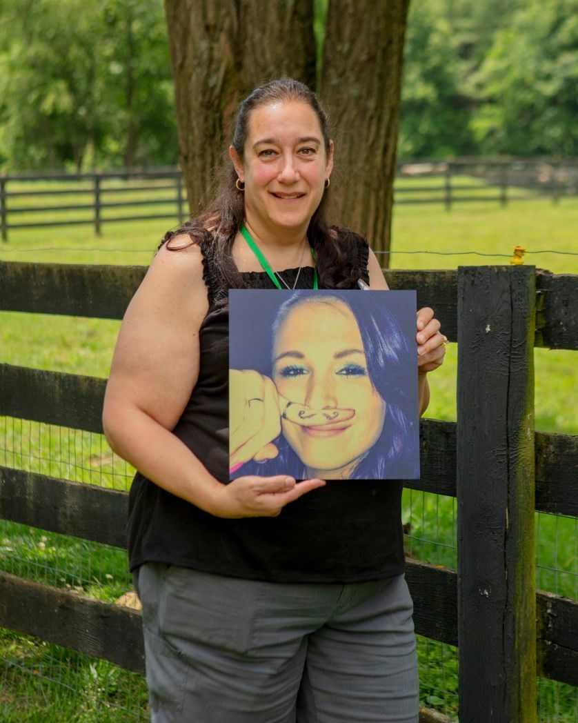 A woman is holding a picture of herself in front of a fence