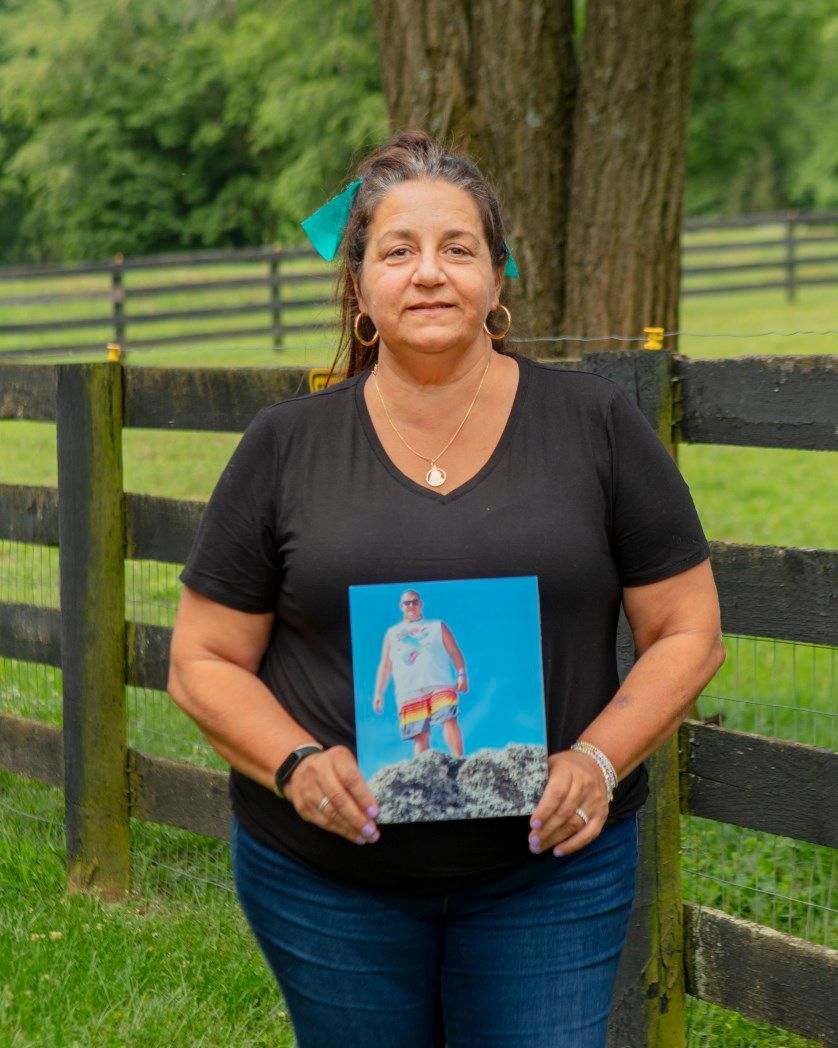 A woman in a black shirt is holding a picture of a man standing on a rock.