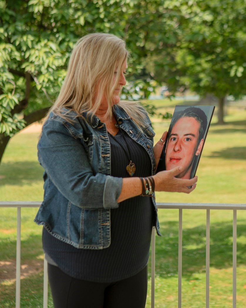 A woman in a denim jacket is holding a picture of a man.