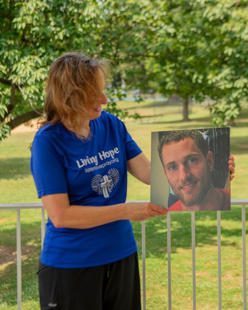A woman in a living hope shirt is holding a picture of a man