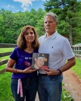 A man and a woman are standing next to each other holding a picture of a man.