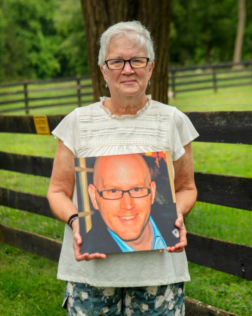 A woman is holding a picture of a man with glasses