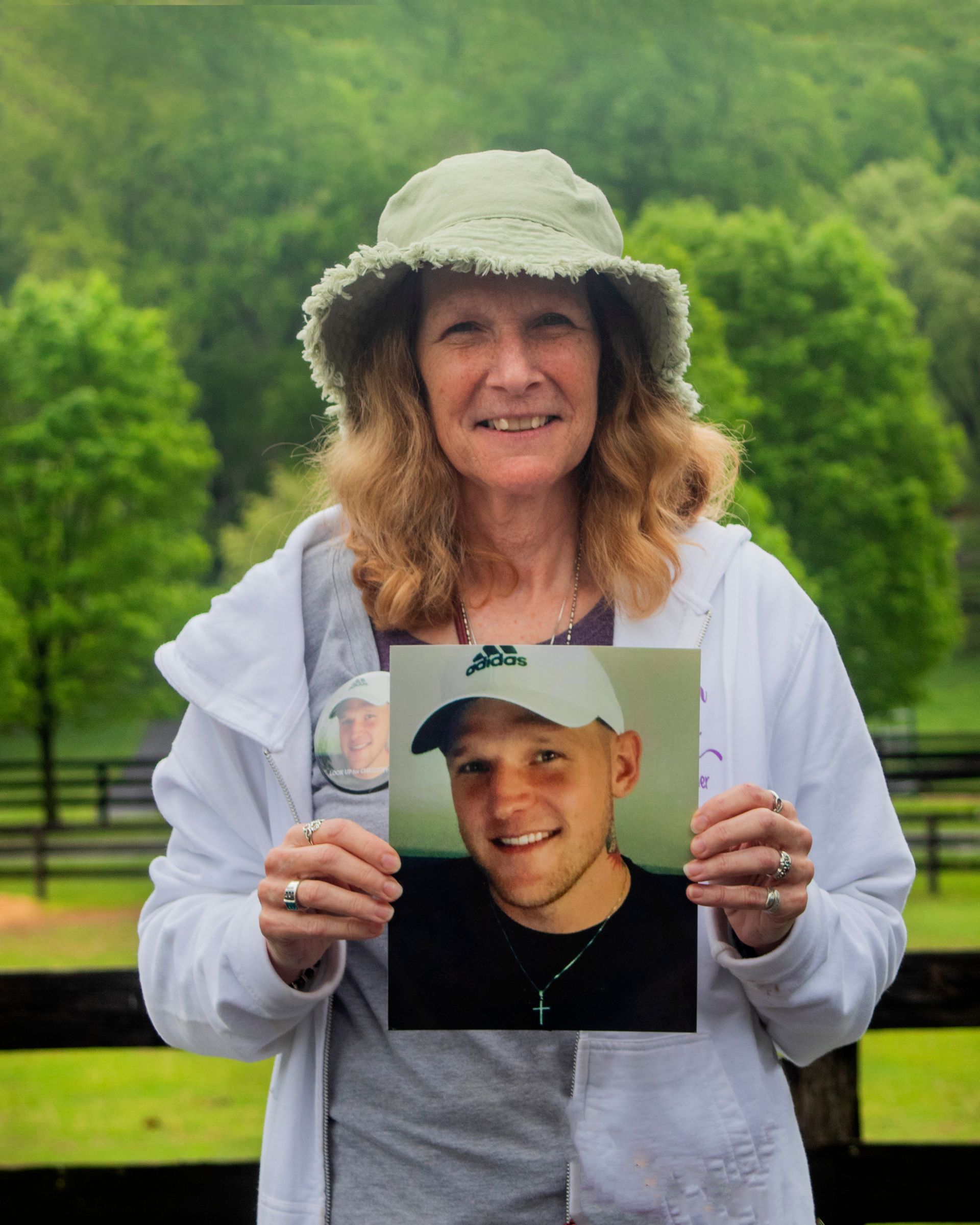 A woman in a hat is holding a picture of her son