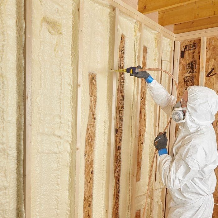 A man in a protective suit is measuring a wall with a tape measure.