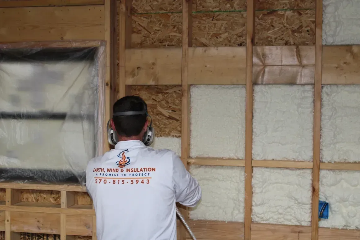 A man is spraying insulation on a wooden wall.