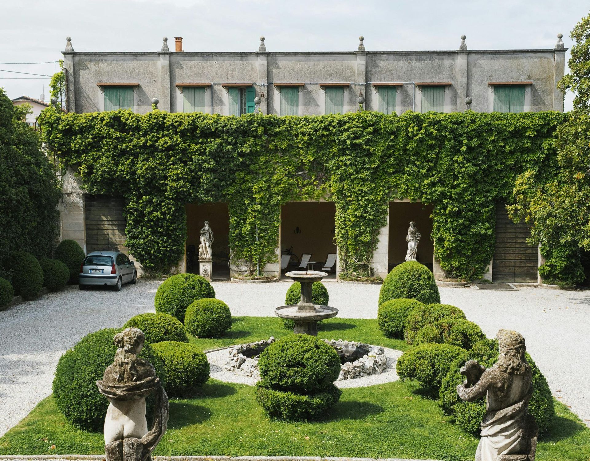 Courtyard with a garden, fountain, sculptures, and a building covered in ivy.