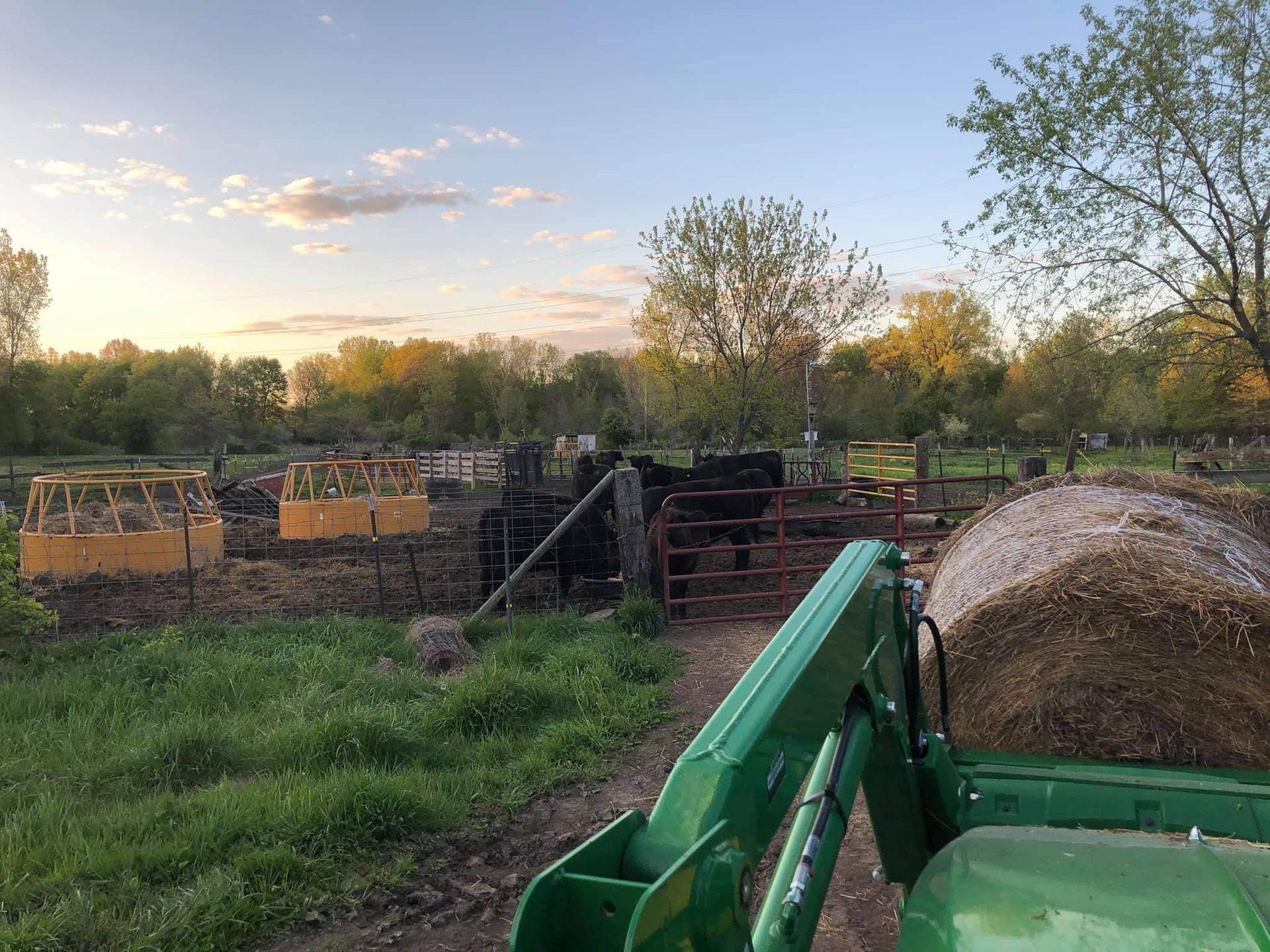 Green tractor near a farm scene, with raised garden beds and trees at sunset.