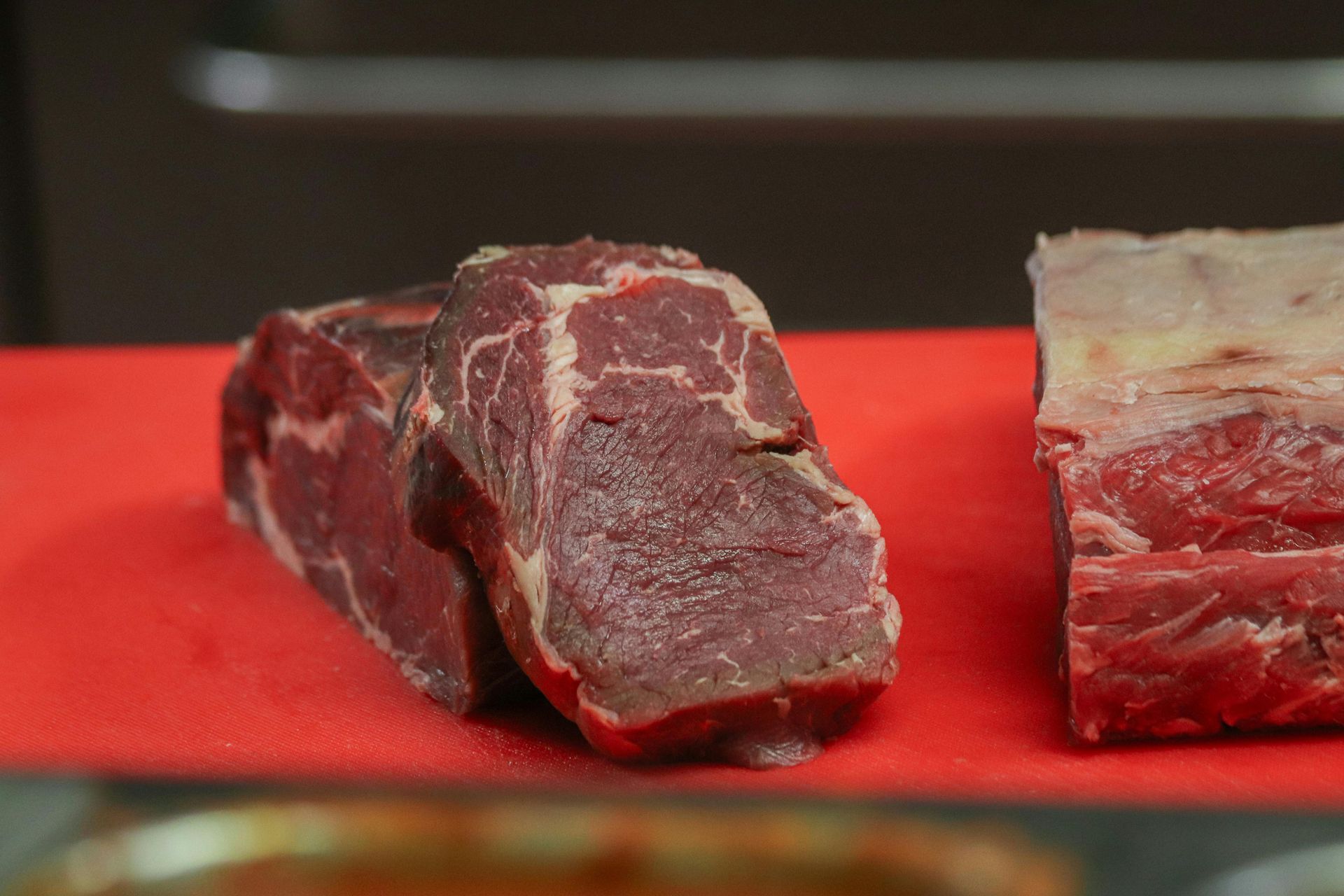 Raw, dry-aged beef cuts on a red cutting board; partially in focus.