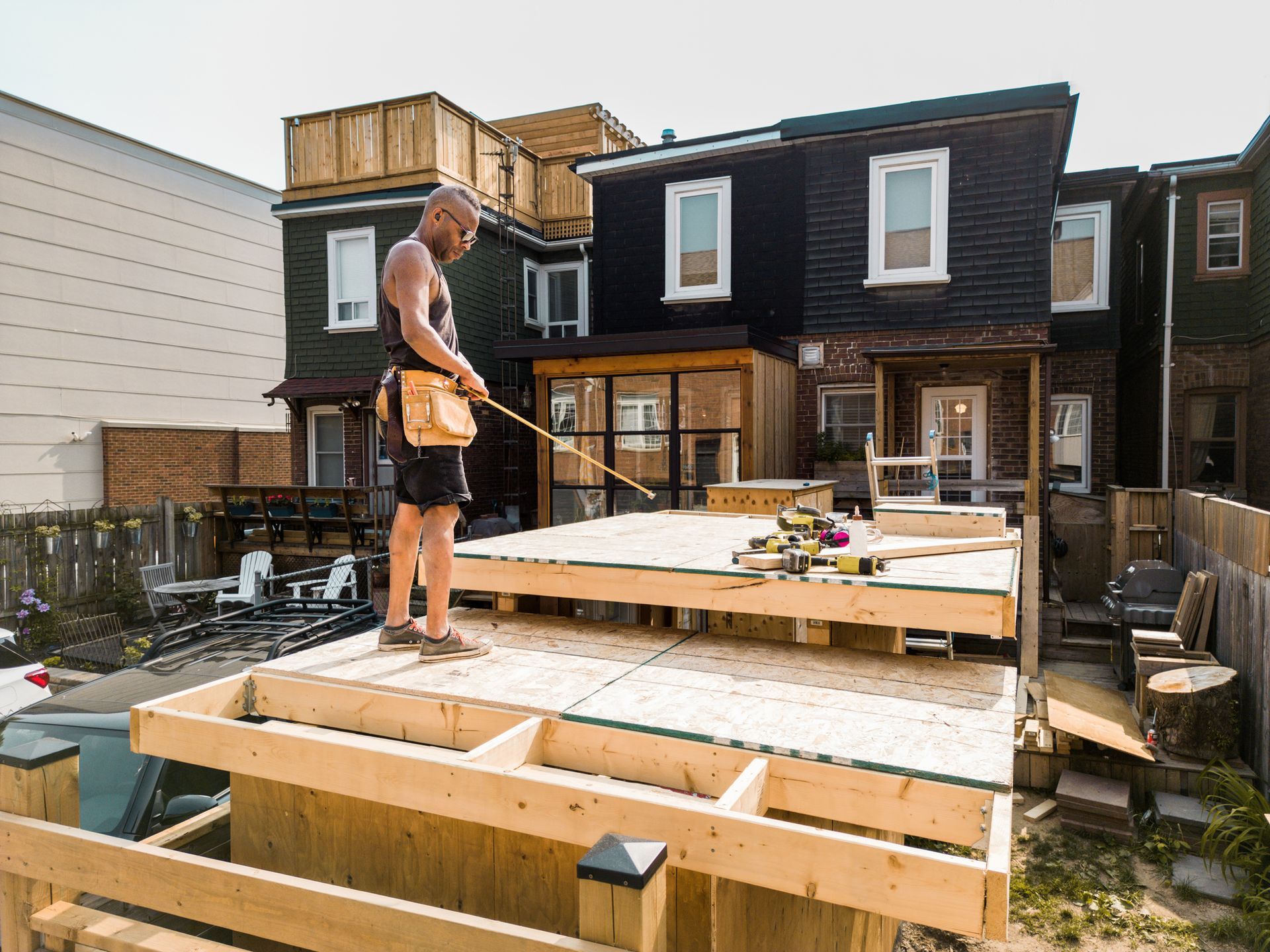 Construction worker building a wooden deck in a backyard. The worker has a tool belt.