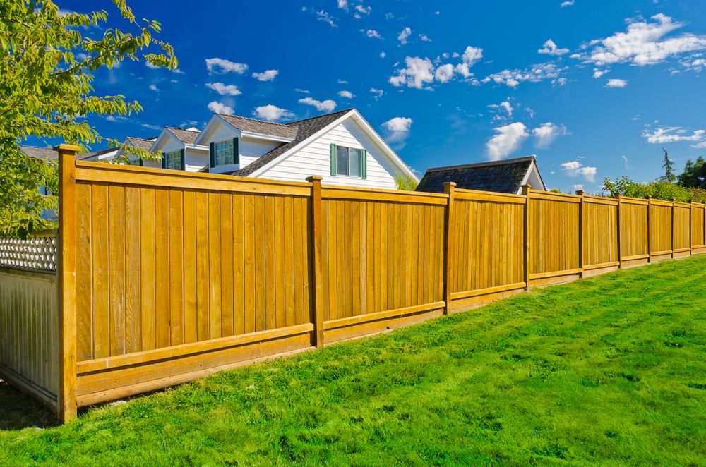 A wooden fence surrounds a lush green lawn in front of a house.