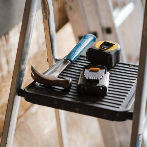 A hammer , tape measure , and battery are on a step ladder.