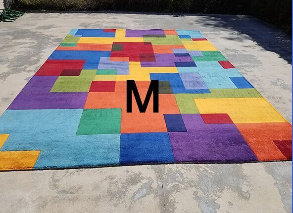 A rectangular area rug with a colorful, multi-shaped geometric block pattern in red, yellow, blue, green, and purple.