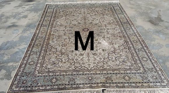 A rug with the letter m on it is sitting on a concrete floor.
