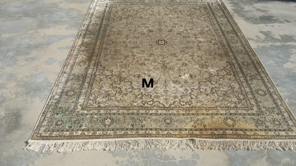 A rug with the letter m on it is sitting on a concrete floor.