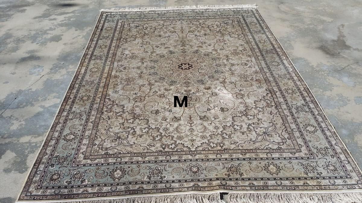 A rug with the letter m on it is sitting on a concrete floor.