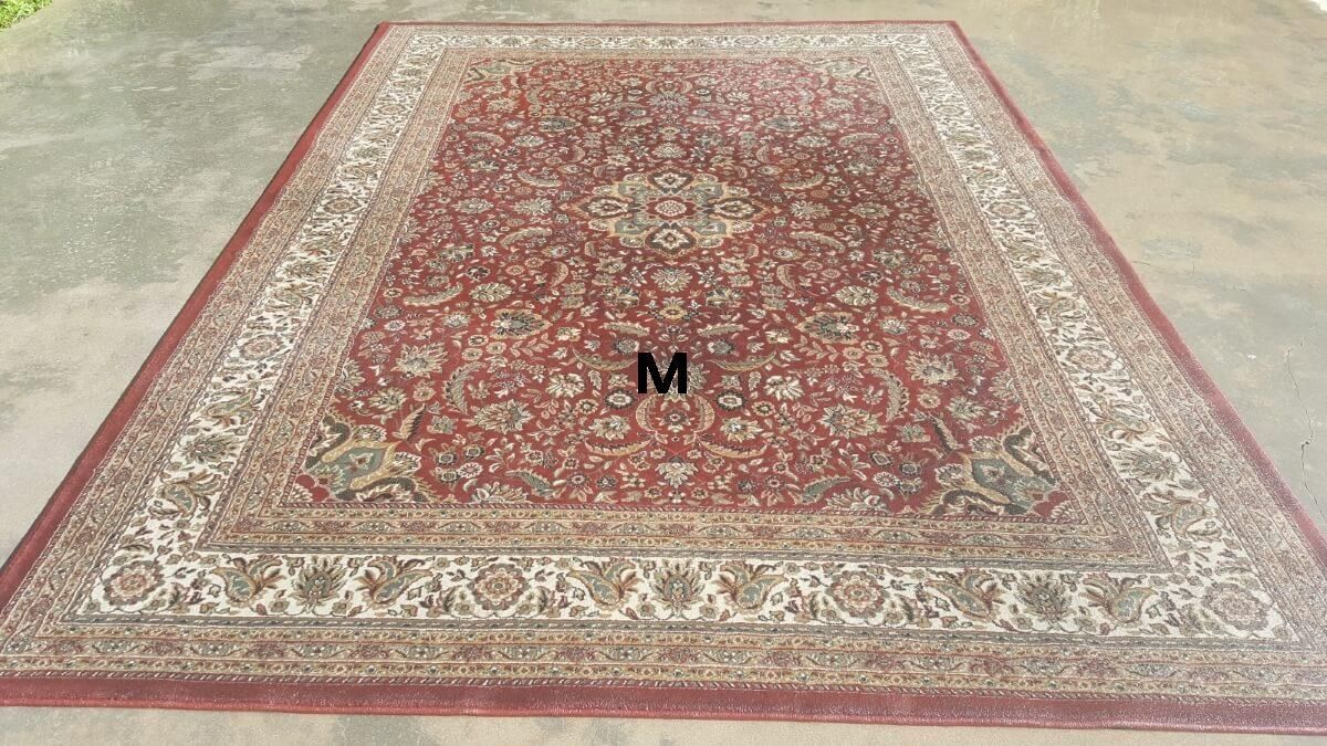 A large rug with the letter m on it is sitting on the ground.