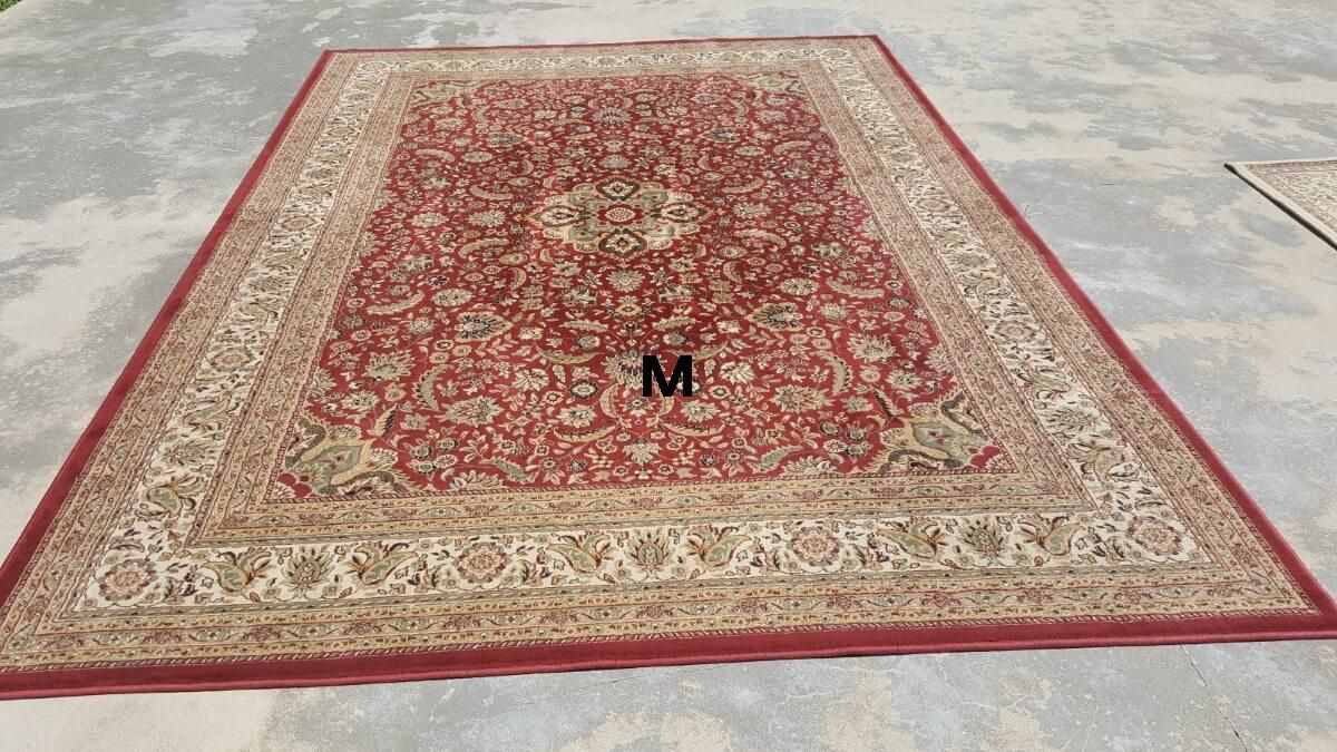A large red and gold rug is sitting on top of a concrete floor.