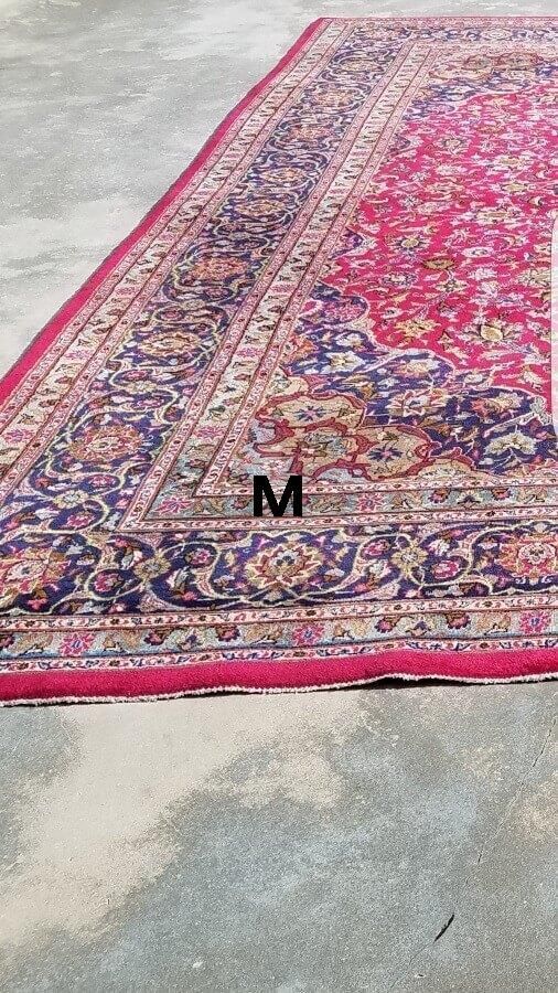 A red rug with a floral pattern is sitting on a concrete floor.