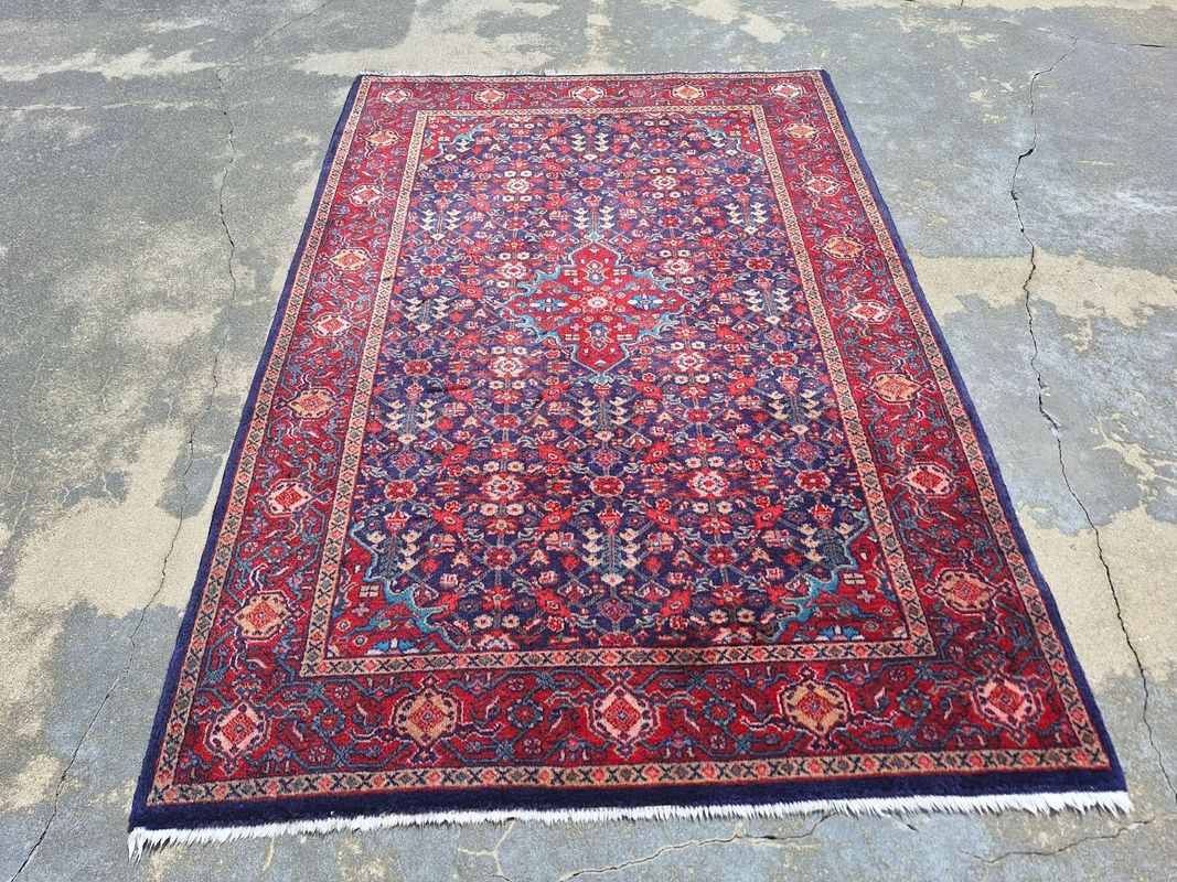 A rectangular rug with a navy blue field, red borders, and intricate, colorful floral and geometric patterns.