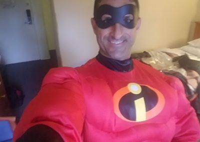 A smiling person wearing an Incredible Hulk costume with a red shirt featuring an orange and yellow logo and a black mask.