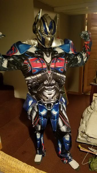 A person wearing a detailed blue, silver, and red Optimus Prime costume from Transformers, posing with flexed arms.