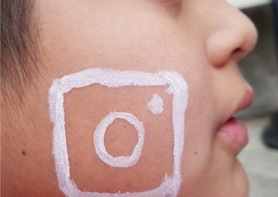 A close-up profile view of a face with the white Instagram logo painted onto the cheek.
