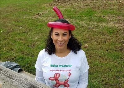 A person wearing a red balloon hat outdoors, smiling at the camera while wearing a 