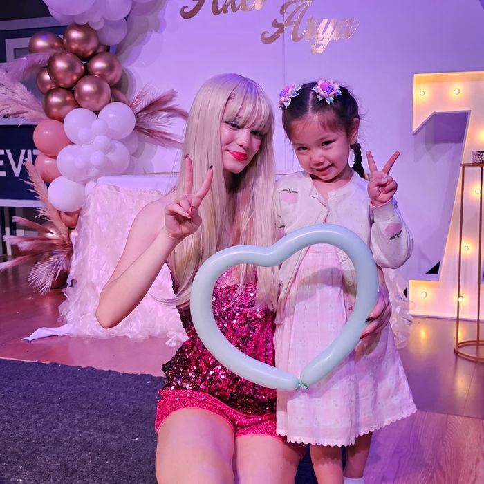 A blonde performer in a pink sequined outfit and a young girl posing with a heart-shaped balloon at a birthday party.
