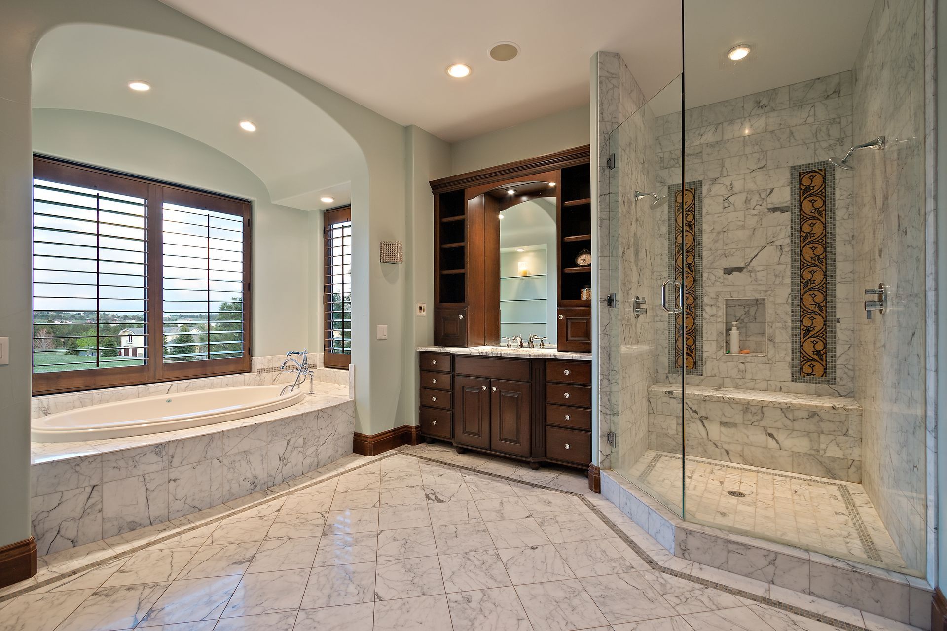 Luxurious bathroom with marble floors, large glass shower, dark wood vanity, and a bathtub by a window.
