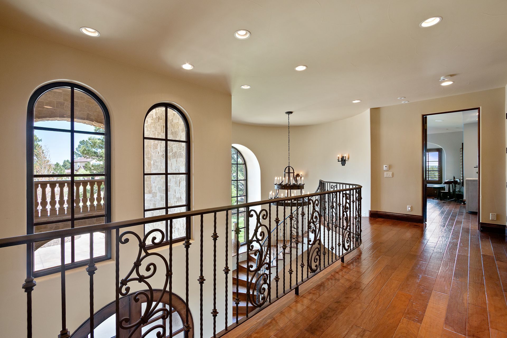 Interior hallway with arched windows, ornate railing, and wooden floors.