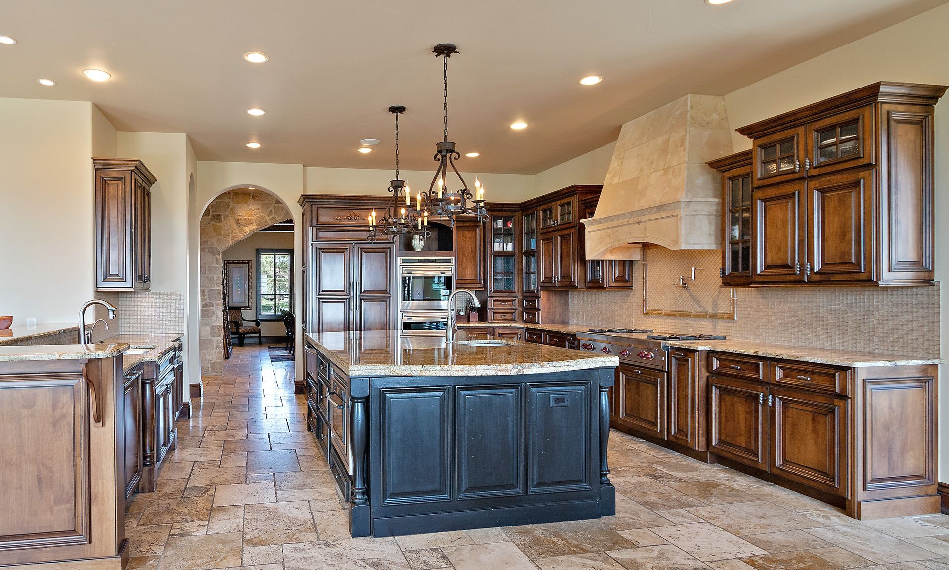 Spacious kitchen with dark wood cabinets, a central island, stone countertops, and a large stone range hood.