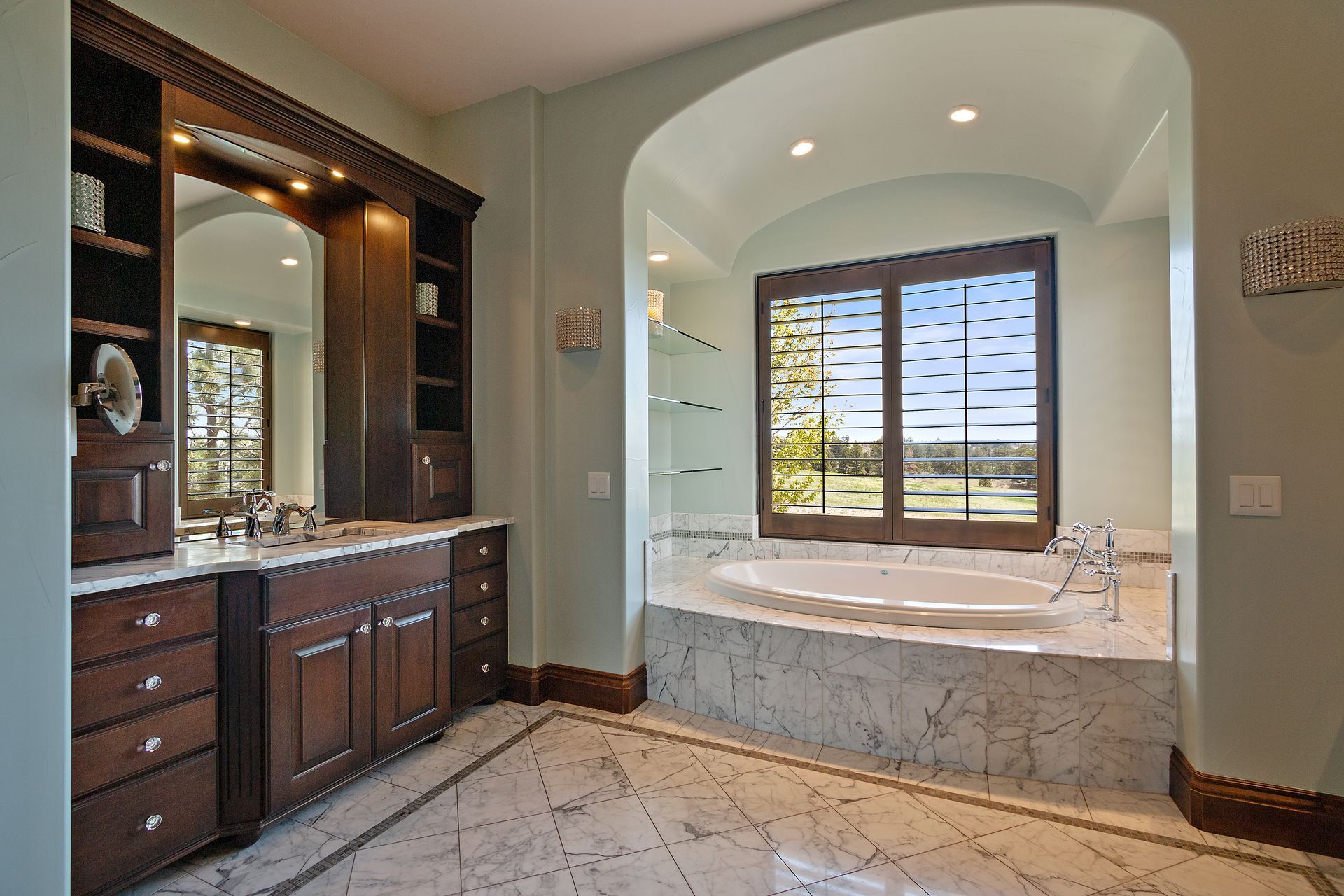 Luxury bathroom with dark wood cabinets, a marble bathtub, and shuttered window.