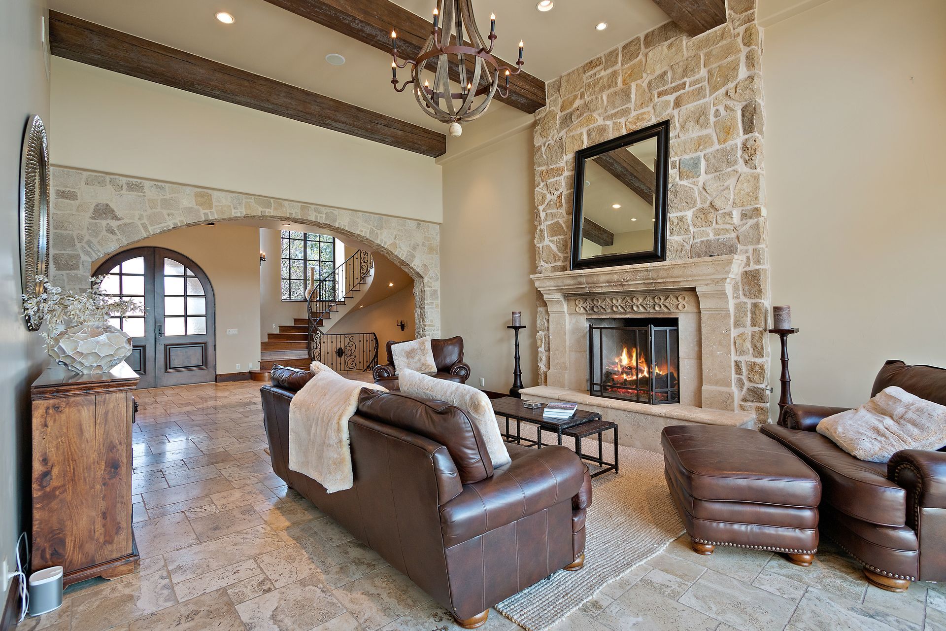 Living room with stone fireplace, brown leather furniture, and arched doorway to a staircase.