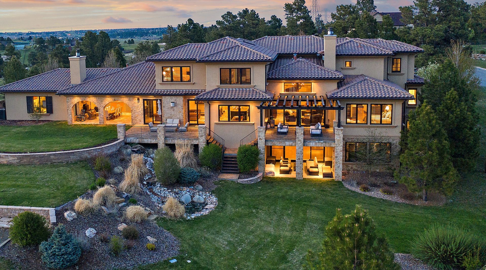 Rear view of a large, luxurious home with a clay tile roof and manicured lawn.
