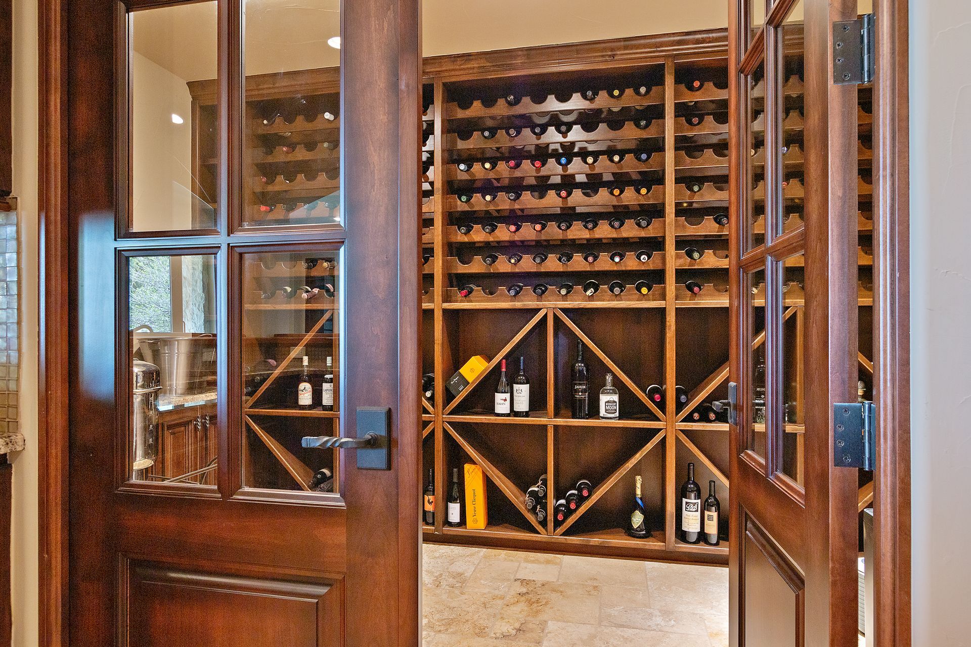 Wooden wine cellar with double doors, filled with bottles on shelves.