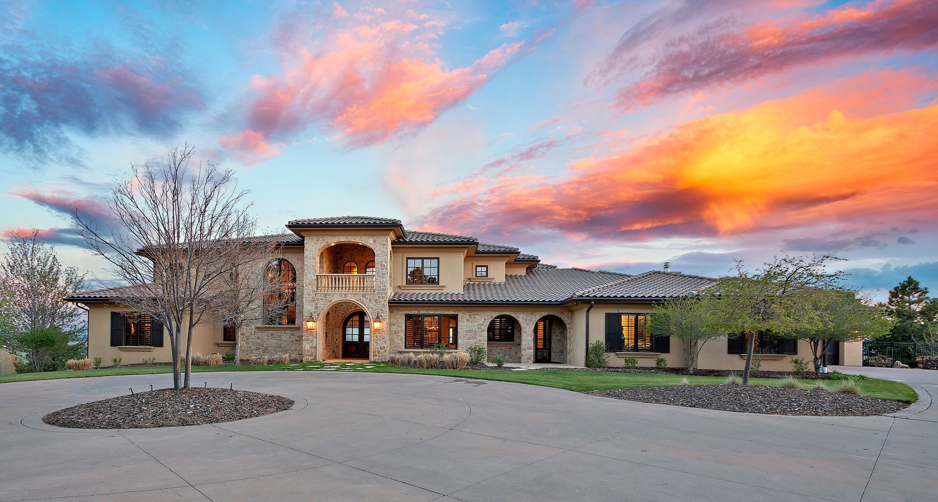 Mansion with beige stucco exterior and arched windows at sunset with colorful clouds.
