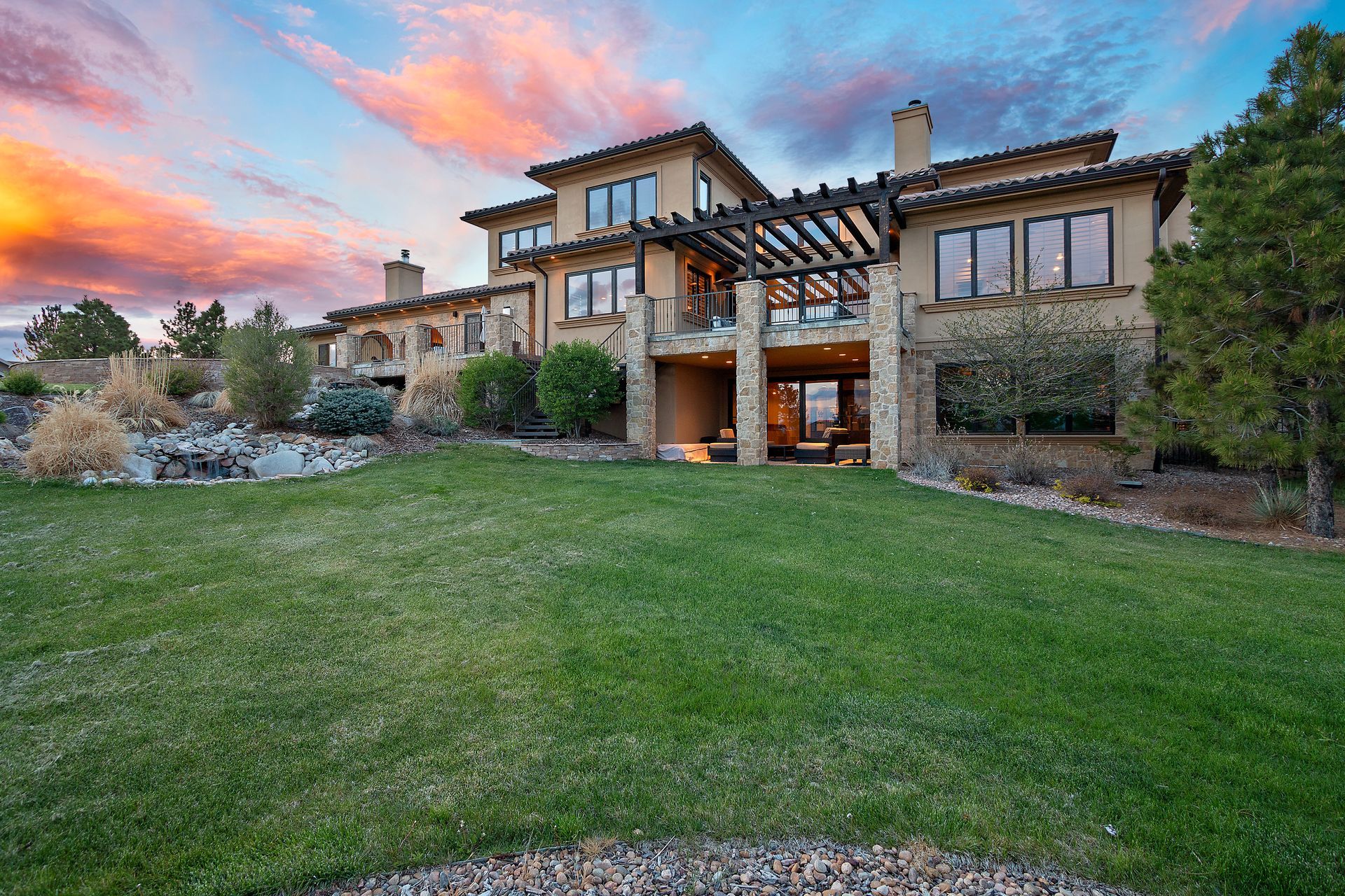 Large, multi-story house with a lawn and colorful sunset.