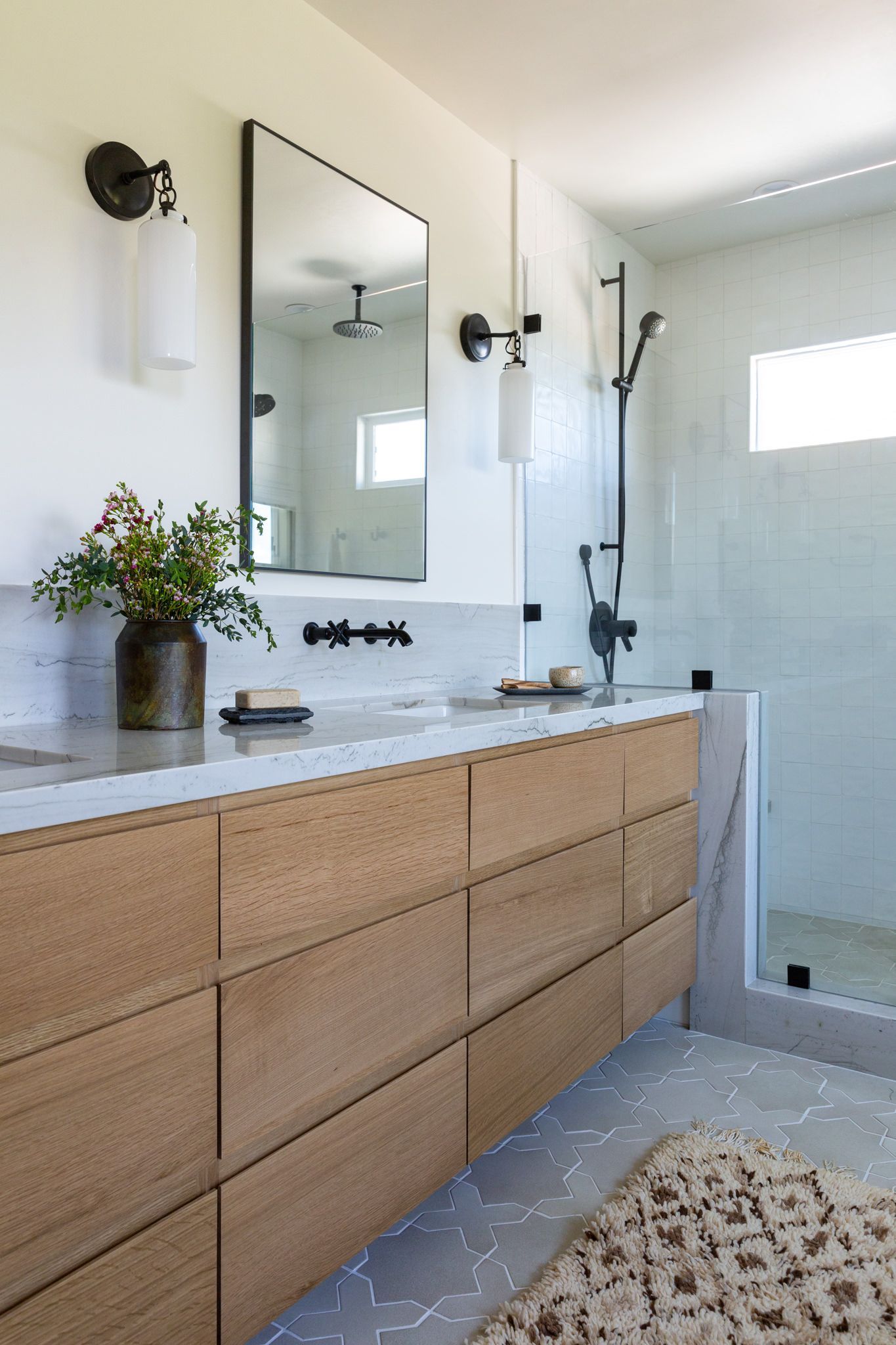 Modern bathroom with wooden vanity, marble countertop, black fixtures, and glass shower.