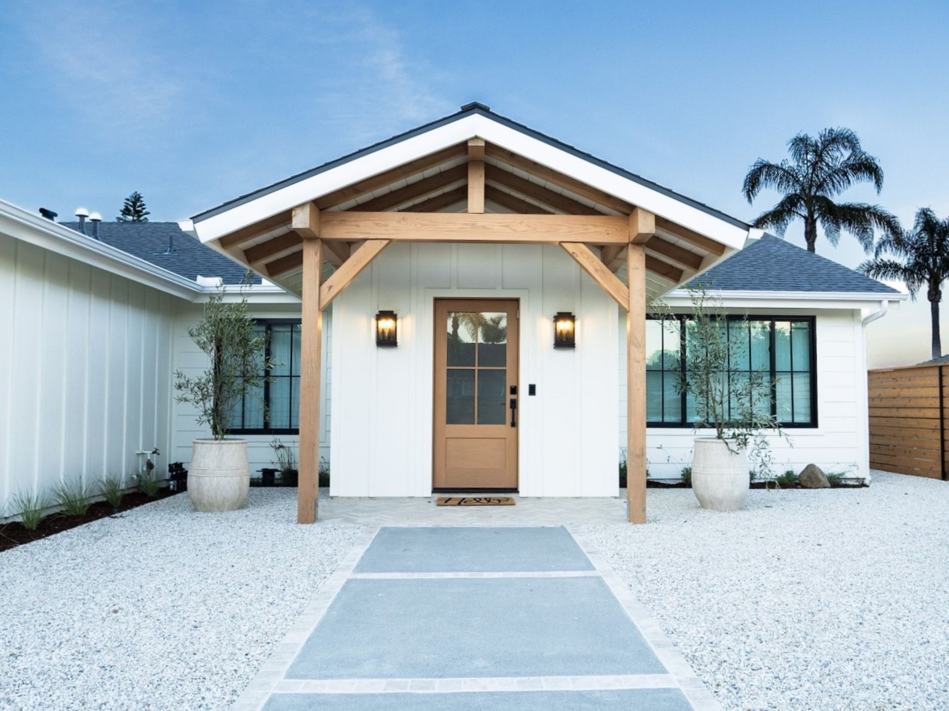 White house with light wooden entryway, concrete path, and gravel yard.