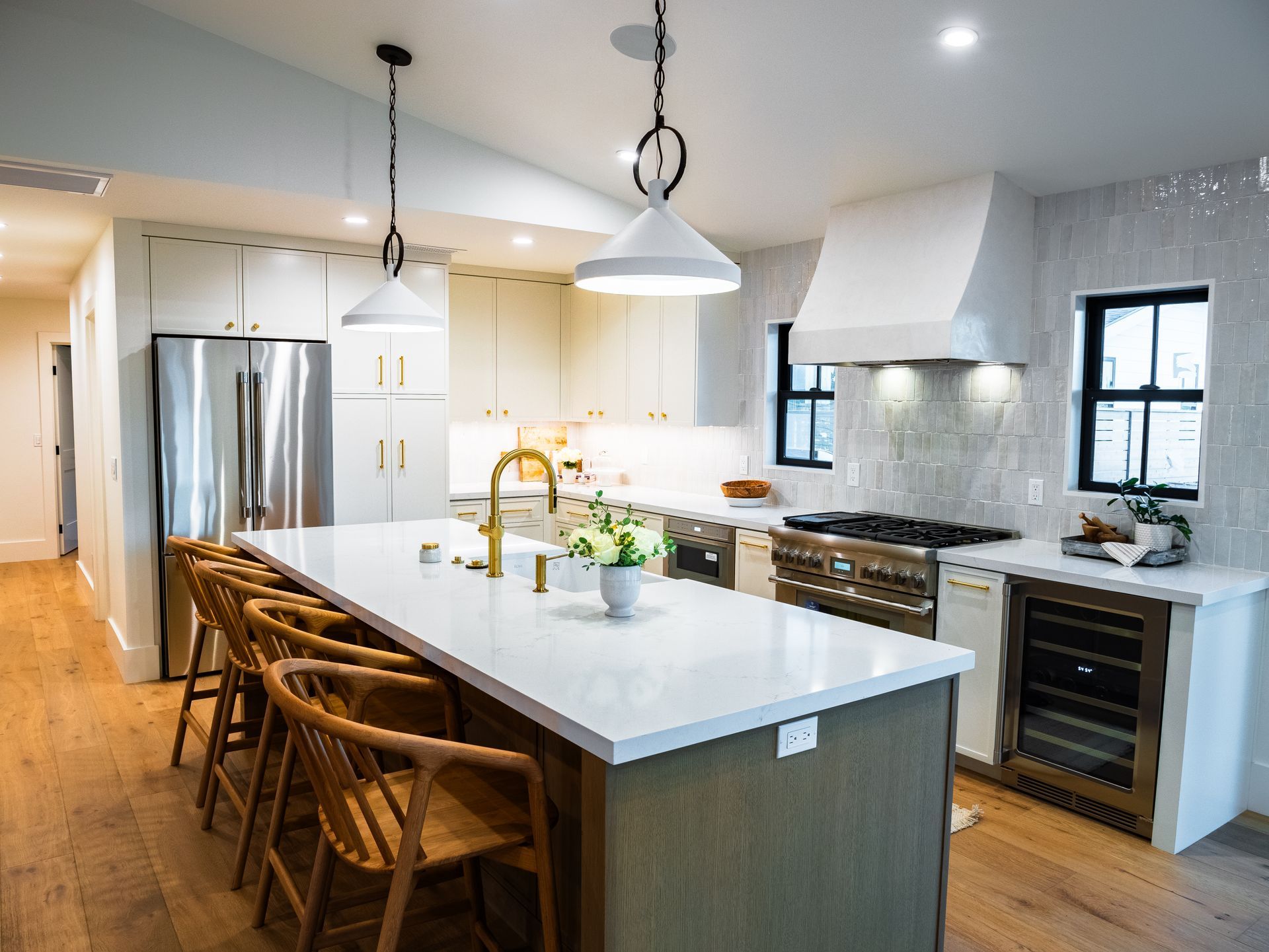 Modern kitchen with large island, white cabinets, stainless steel appliances, and wooden chairs.