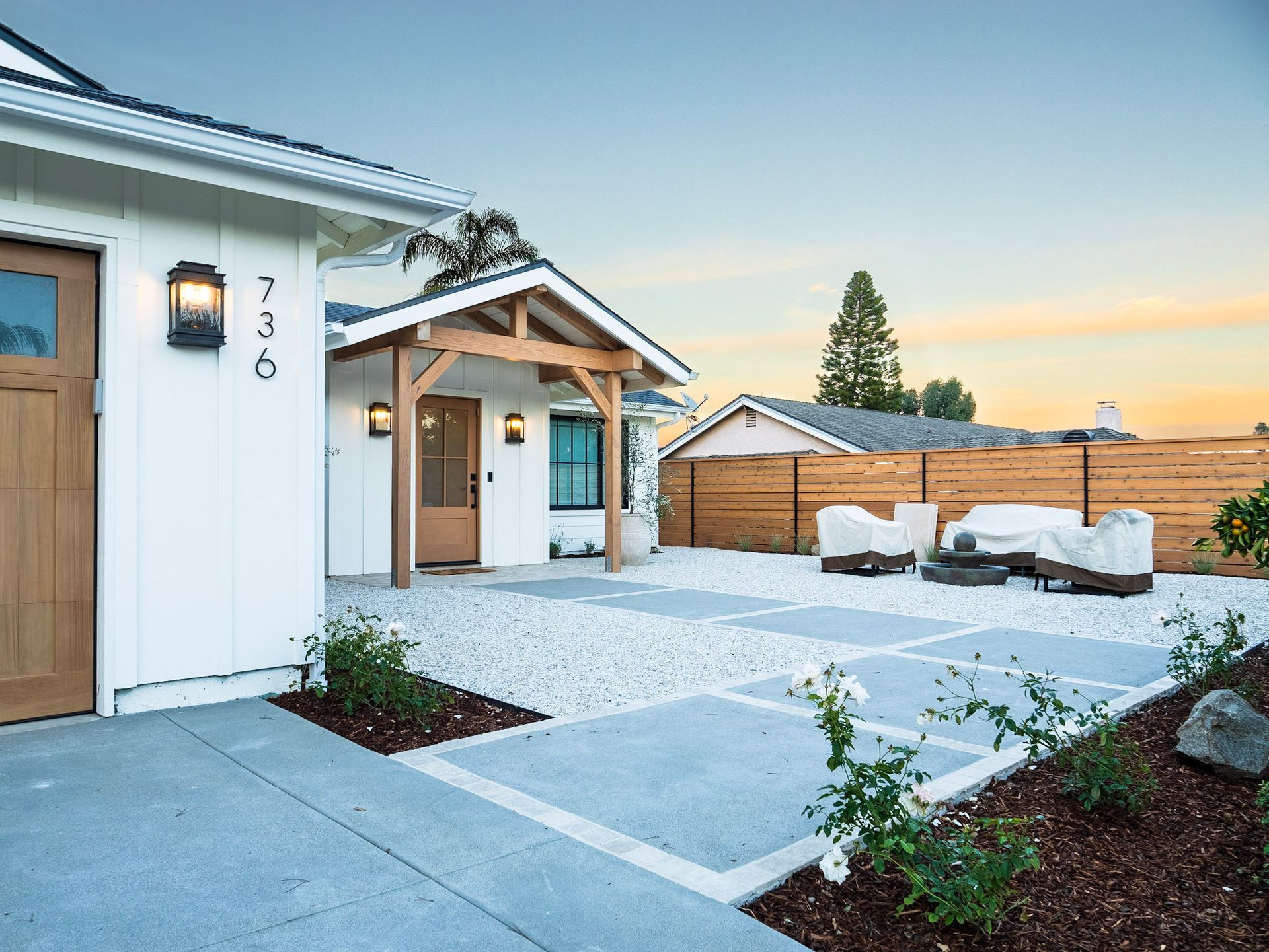 Modern white house with gravel yard, patio squares, wooden door/trim, and landscaping.