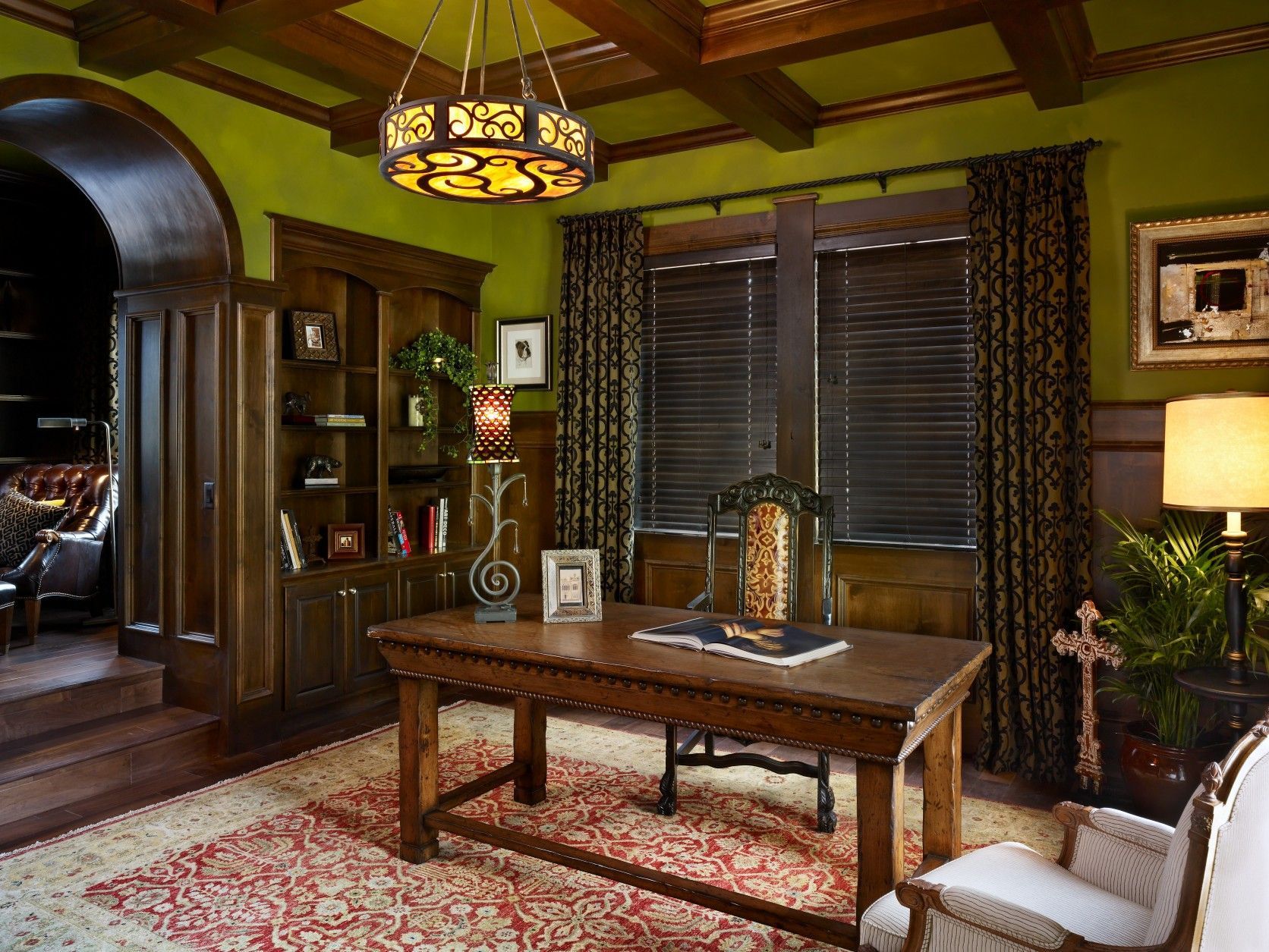 Elegant study with green walls, wooden desk, bookshelves, and patterned rug.