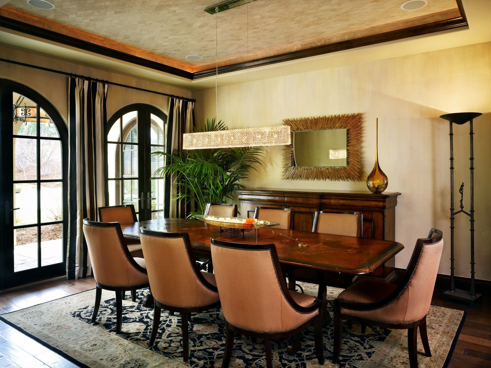 Formal dining room: dark wood table and chairs, buffet, patterned rug, arched windows, and decorative ceiling.