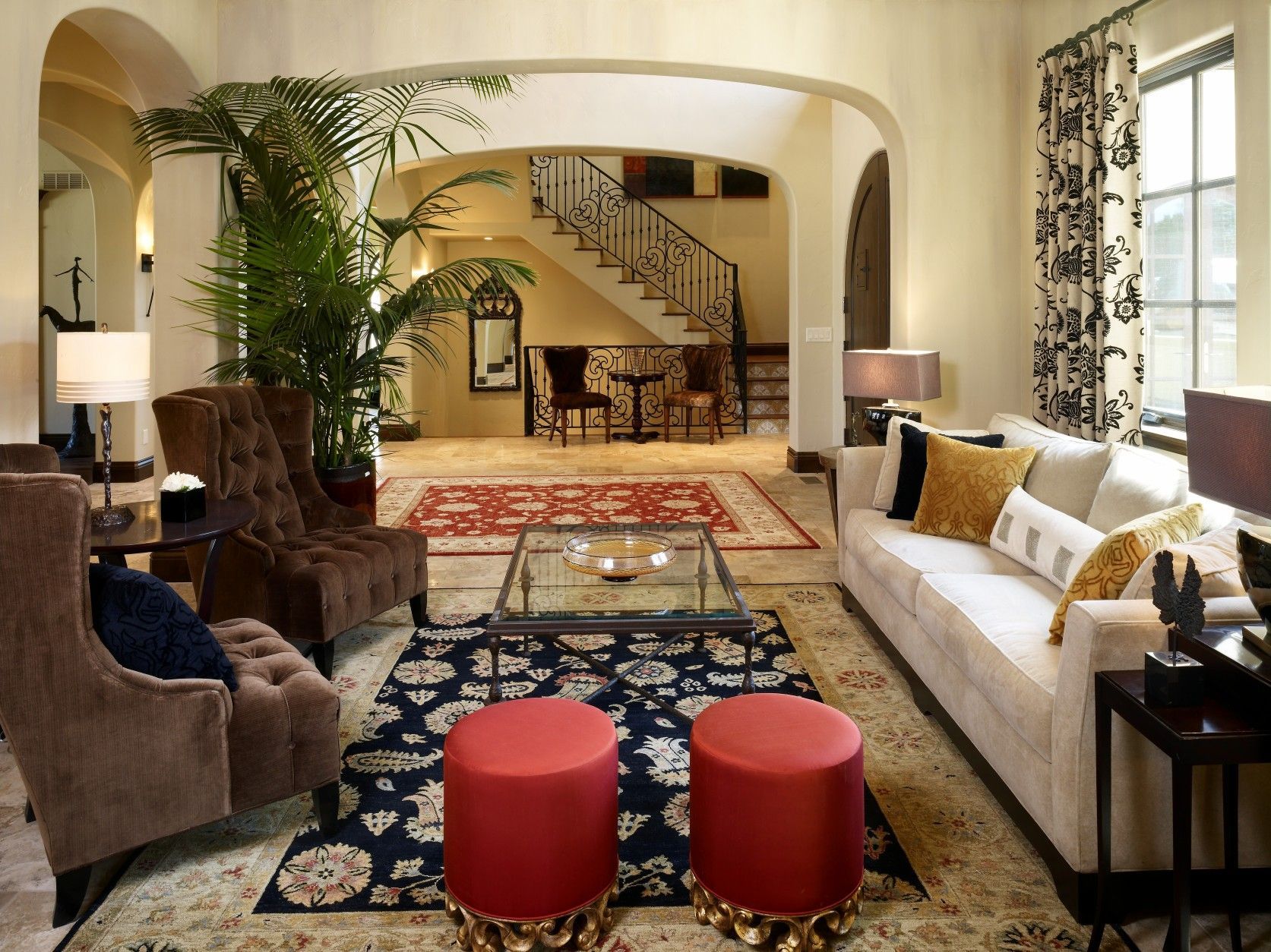 Living room with brown armchairs, white sofa, red ottomans, and staircase.