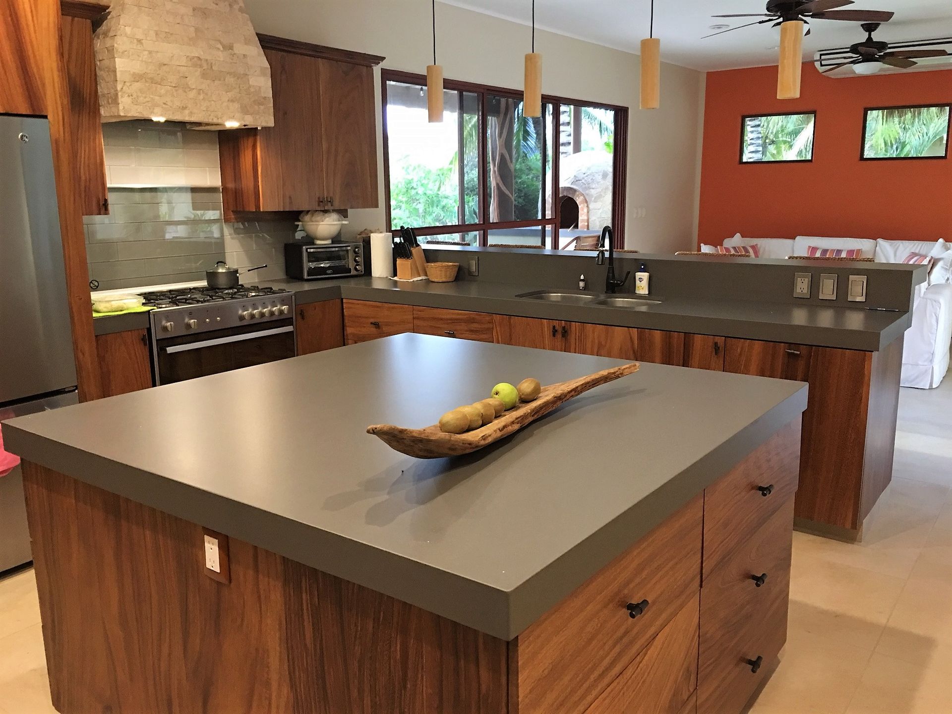 A modern kitchen with a dark gray countertop, wooden cabinets, and an orange accent wall.