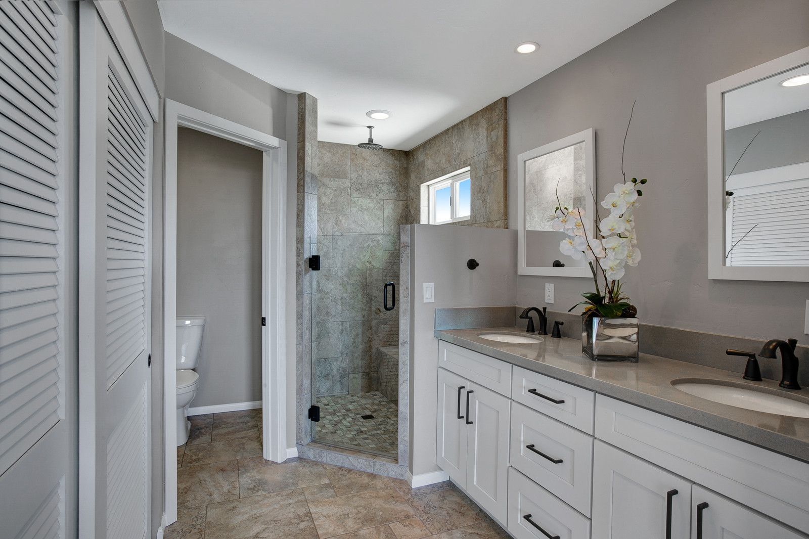 A modern bathroom with gray walls, a walk-in shower, and a double vanity with white cabinets.