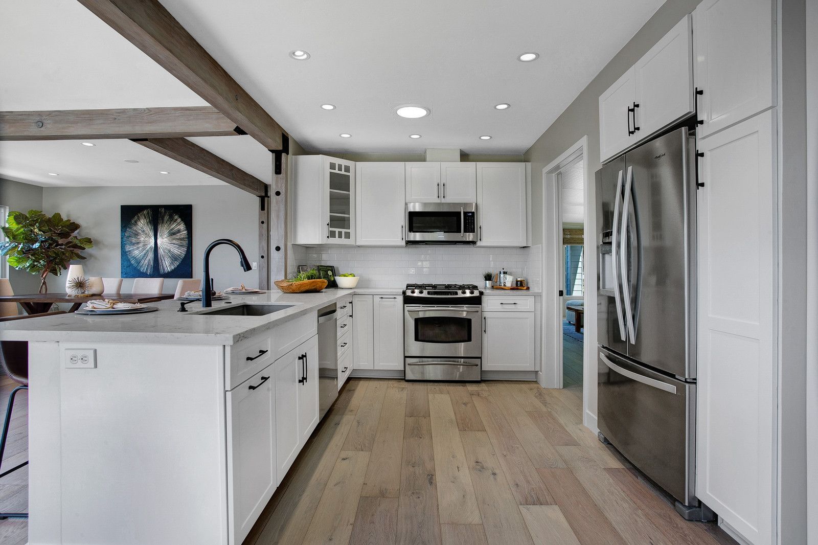 Modern white kitchen with stainless steel appliances and light wood floors.