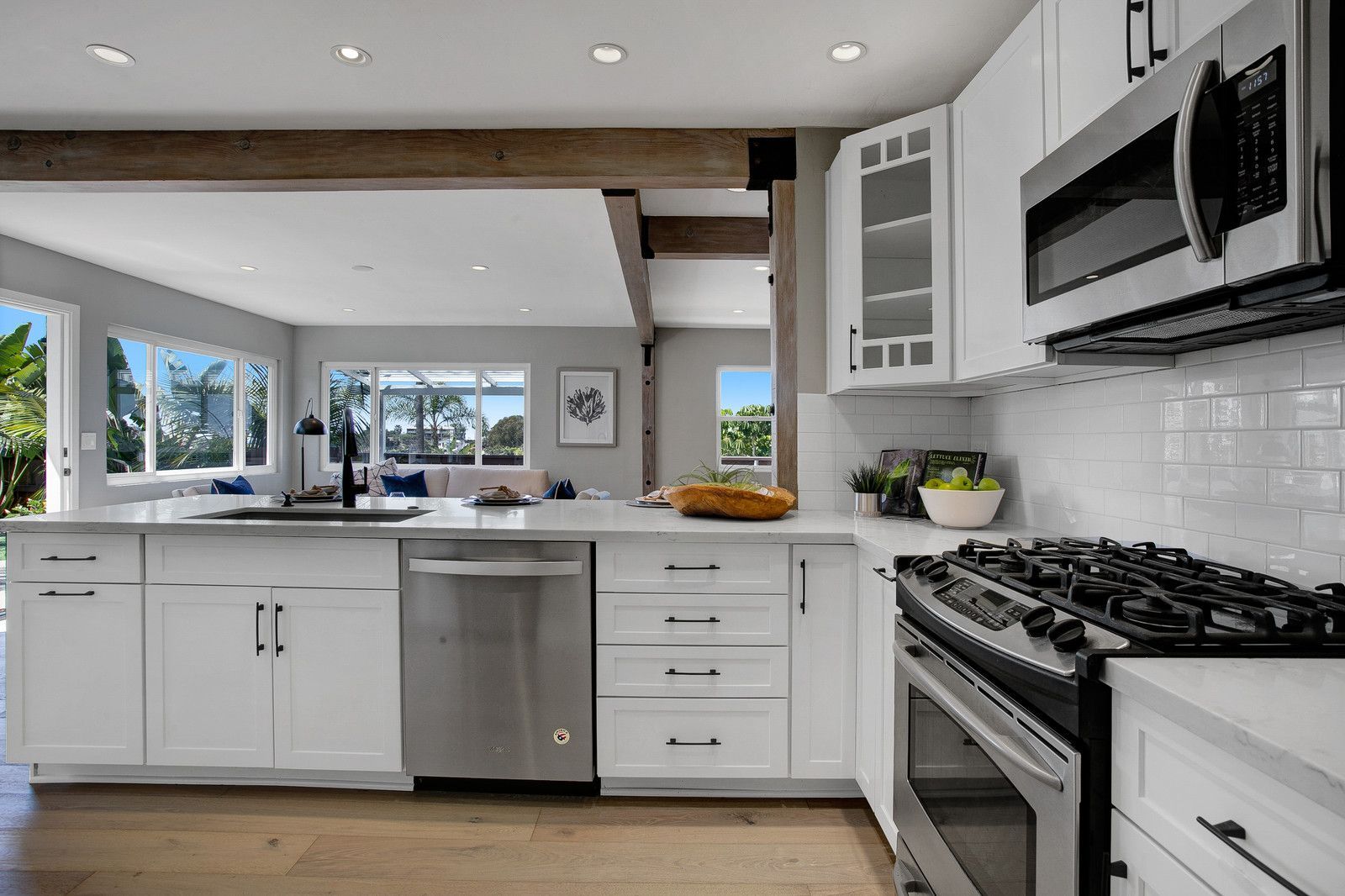 Bright kitchen with white cabinets, stainless steel appliances, and view to living area.
