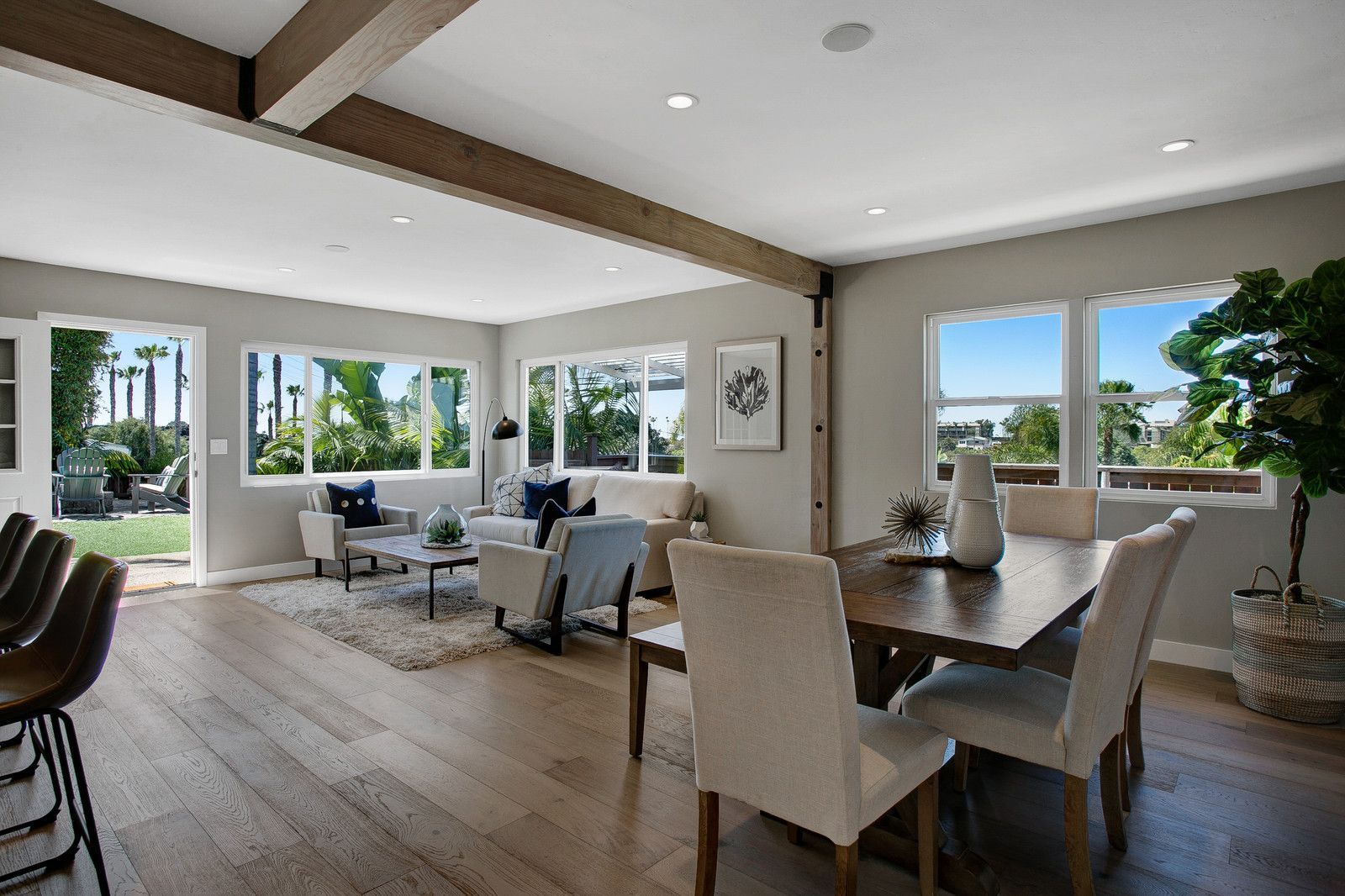 Open-concept living and dining area with light wood floors, windows, and a dining table with chairs.