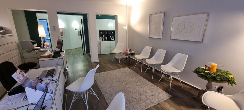 Ein Wartezimmer mit weißen Stühlen und einem Schreibtisch.